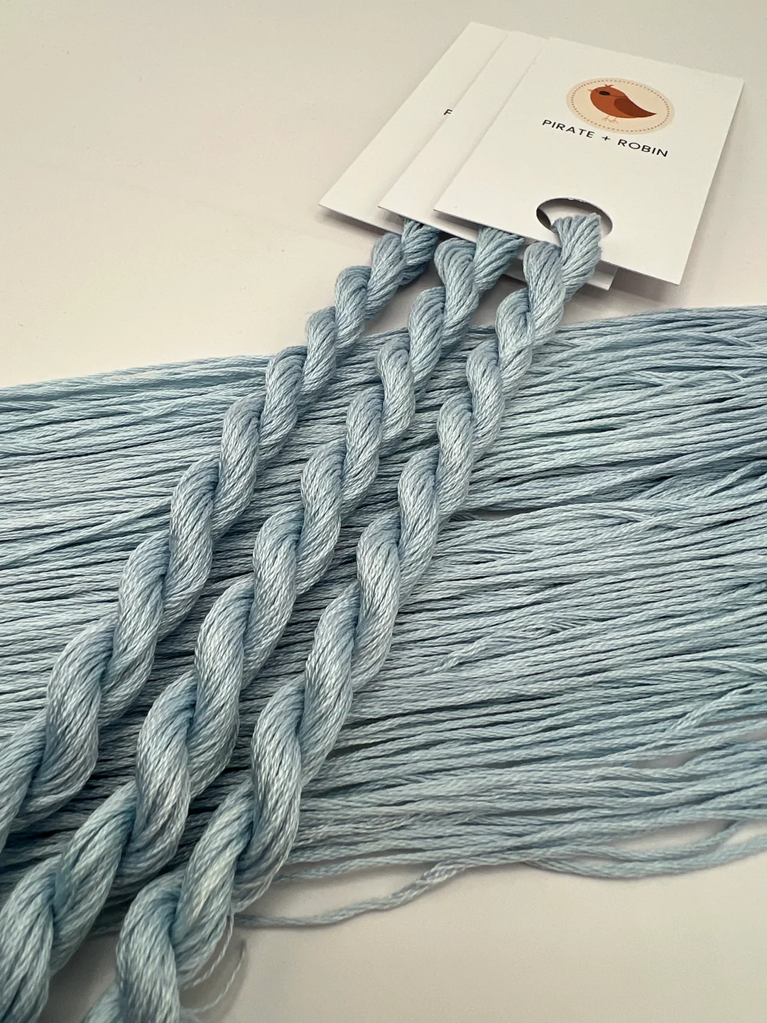 Light blue thread skeins with a brand card in the background on a light surface