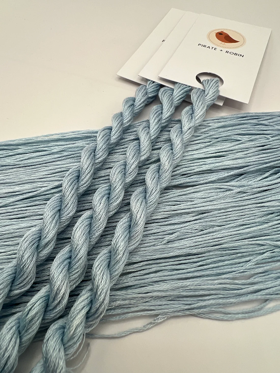 Light blue thread skeins with a brand card in the background on a light surface