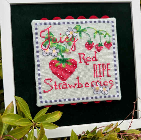 Cross-stitched piece with strawberries and text on a black background