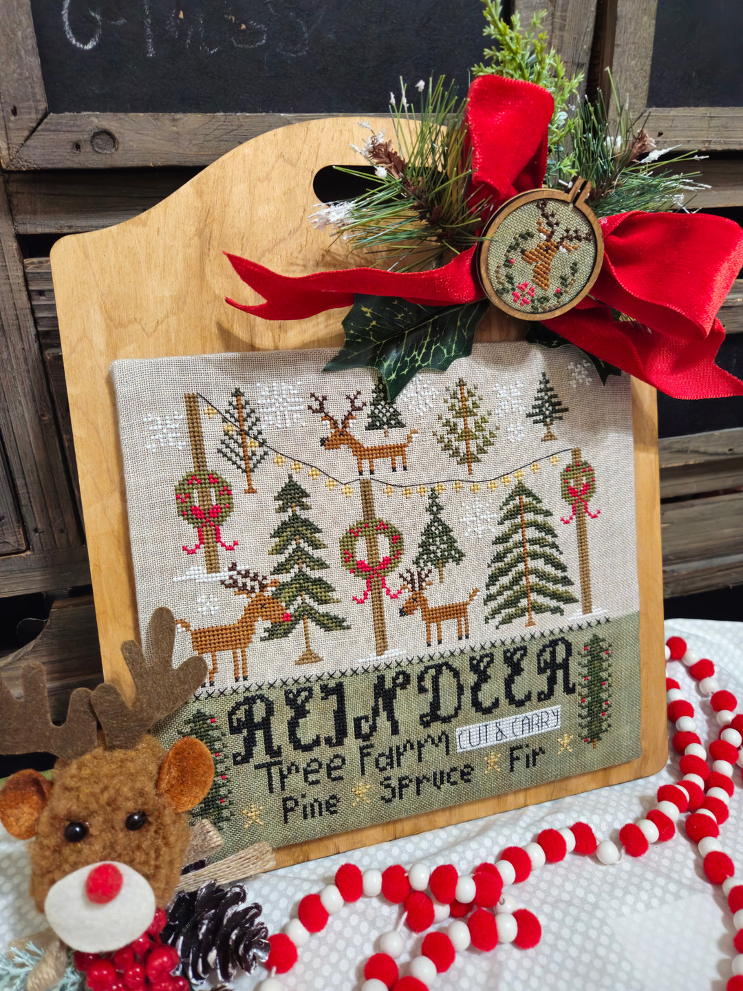 Decorative cross-stitched panel with reindeer and trees, surrounded by festive elements like a red bow and candy canes.