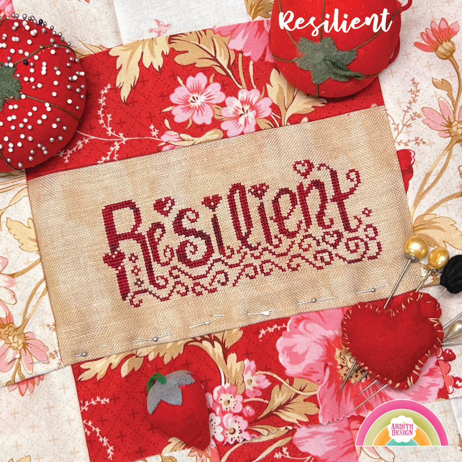 Cross-stitch needlework with the word 'Resilient' written in a decorative font, surrounded by floral patterns on the fabric.