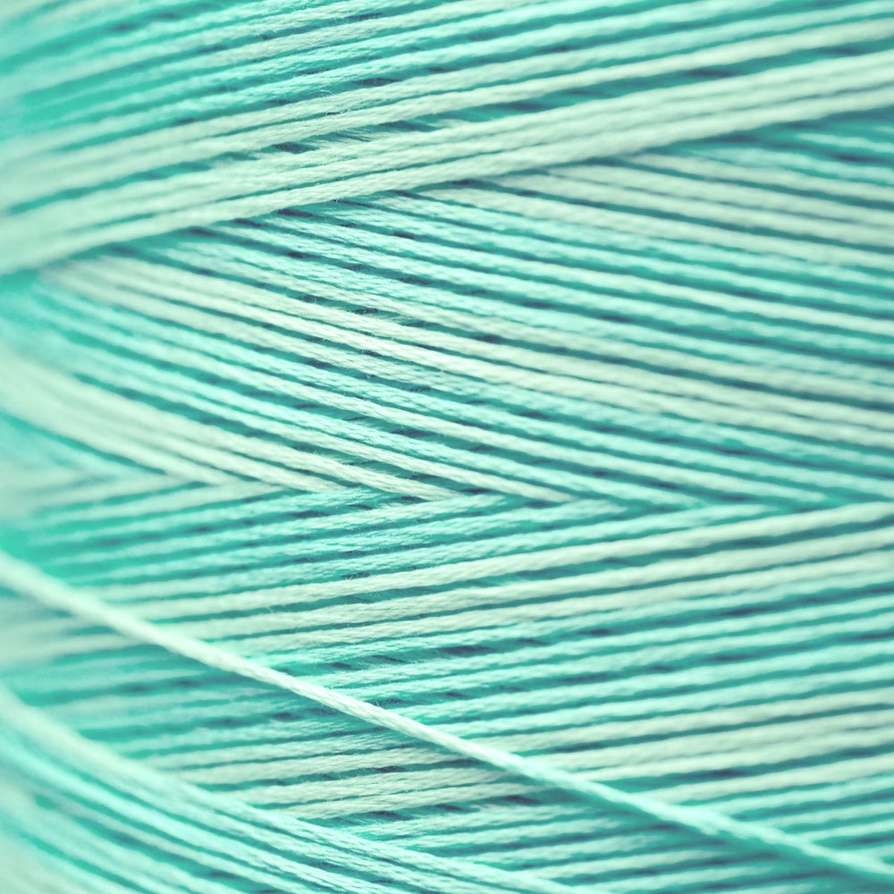A close-up of mint green and light aqua yarn strands wound together, showing the texture and color of the thread.