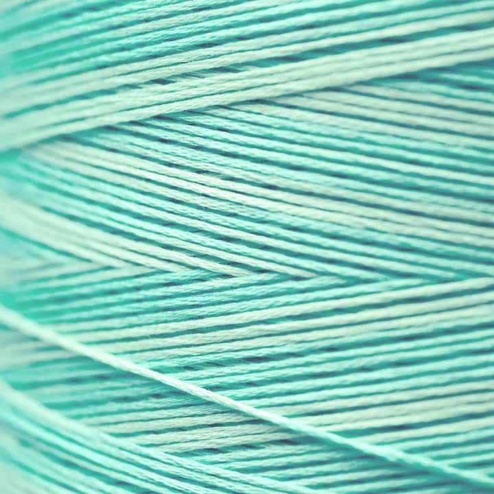 A close-up of mint green and light aqua yarn strands wound together, showing the texture and color of the thread.