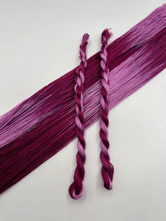 Two braided floss skeins in a gradient of purple on a light gray background