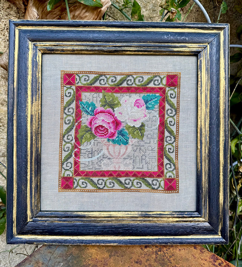 Framed cross-stitched piece with a floral design on a textured fabric background.