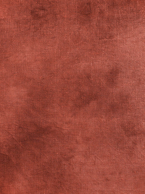 A close-up of a textured fabric or material swatch in a warm rust or terracotta color, filling the entire frame.