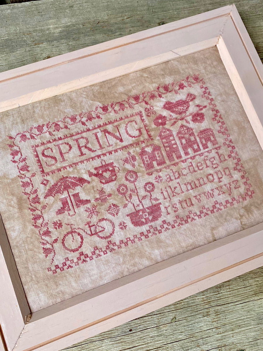 Cross-stitched piece with 'SPRING' text and decorative elements on a wooden surface
