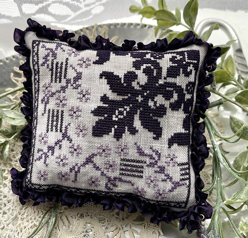 Decorative pillow with black floral pattern on a white background, surrounded by green leaves.