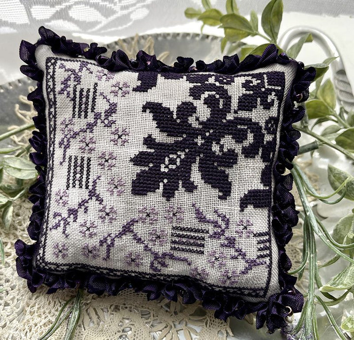 Decorative pillow with black floral pattern on a white background, surrounded by green leaves.