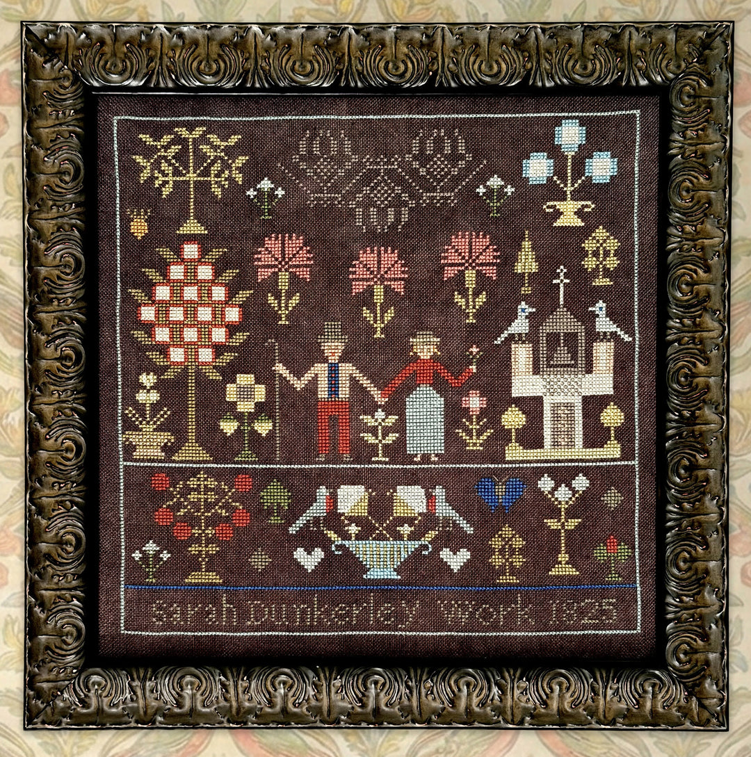 Decorative needlepoint with floral and architectural designs, framed in ornate gold frame.