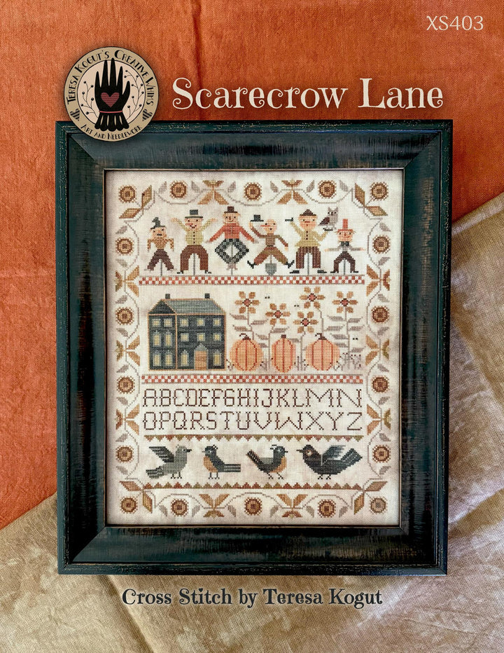 Cover of a cross stitch pattern titled 'Scarecrow Lane' by Teresa Kogut, showing a framed folk-style stitched design with figures, a house, pumpkins, alphabet text, and birds on a warm orange and beige background.