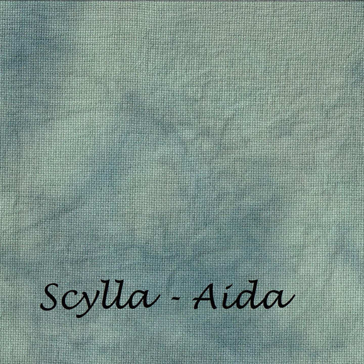A square fabric swatch with a mottled, textured pattern in shades of dusty teal, blue, and gray, featuring the text 'Scylla - Aida' printed in black cursive at the bottom.