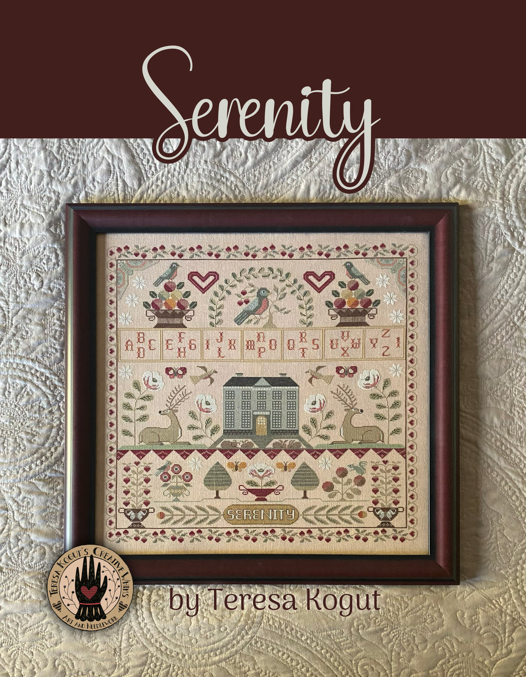 Framed cross-stitch pattern titled 'Serenity' by Teresa Kogut on a textured wall.