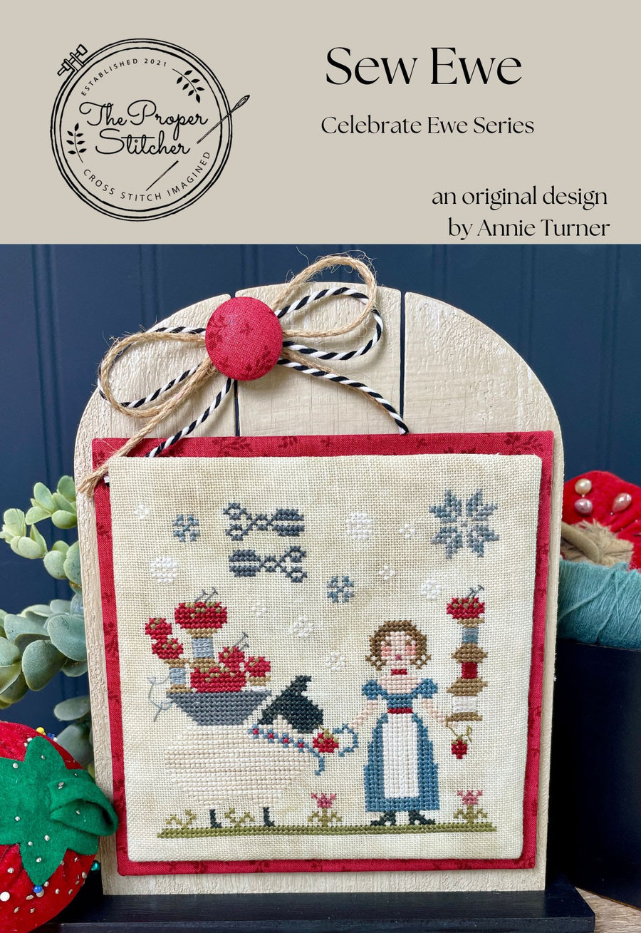Cross-stitched design with decorative elements on a wooden stand, featuring 'Sew Ewe' branding.