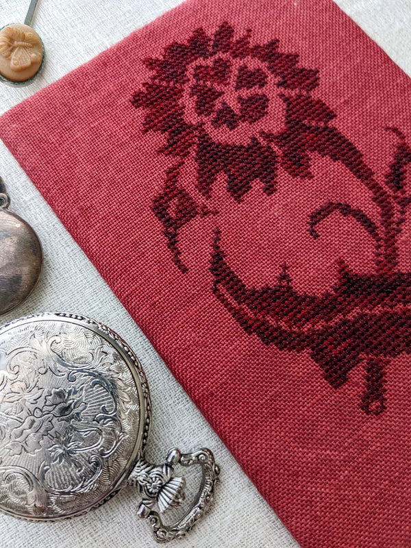 Red fabric with embroidered design of a horse, surrounded by vintage coins and jewelry on a textured surface.