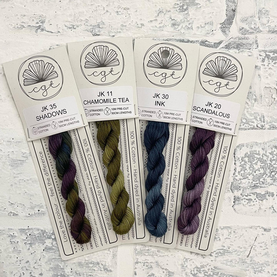 A collection of four skeins of variegated threads in different shades of green, blue, purple, and brown, labeled as 'Stitchers Palette' by Cottage Garden Threads. Colors include Shadows, Chamomile Tea, Ink, and Scandalous.