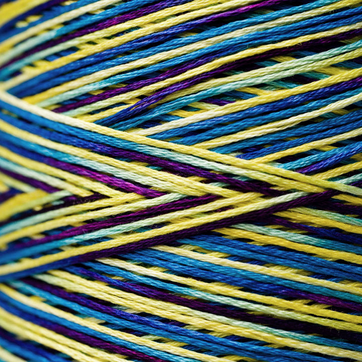 Close-up of variegated yarn strands in bright yellow, blue, teal, and purple crossing over each other.