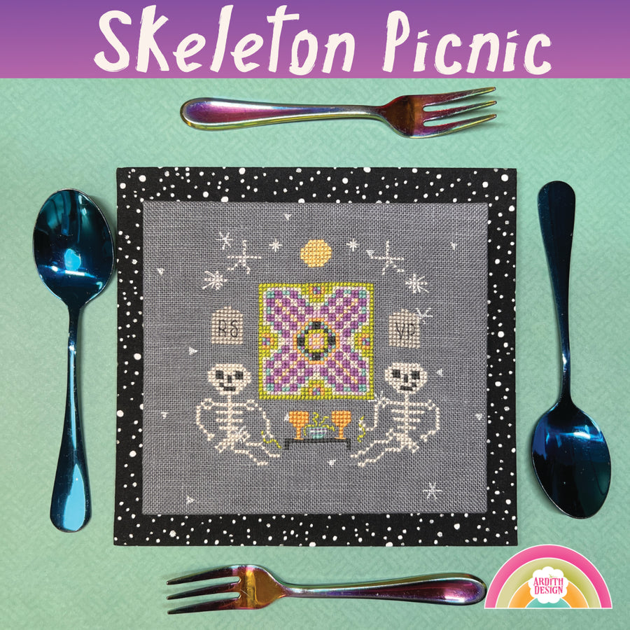 A decorative skeleton picnic blanket with colorful stylized tombstone print, displayed on a table with cutlery.