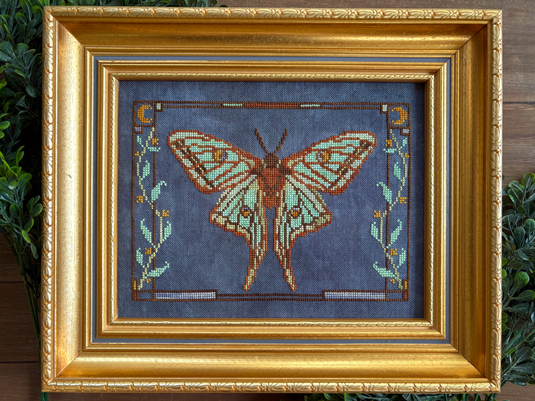 Framed cross-stitched butterfly on a blue background with gold frame