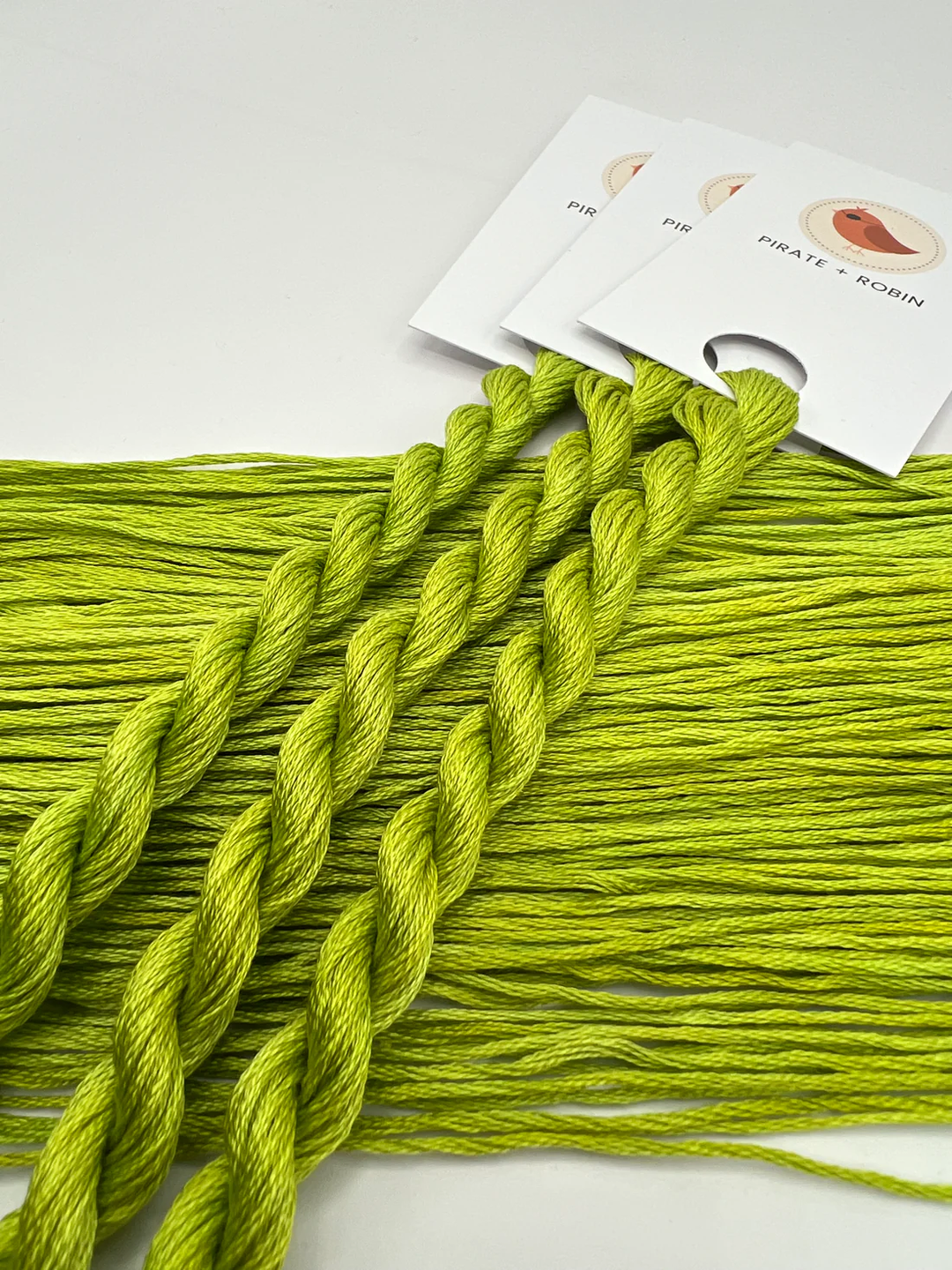 Three skeins of green embroidery floss on a white background with a brand label.
