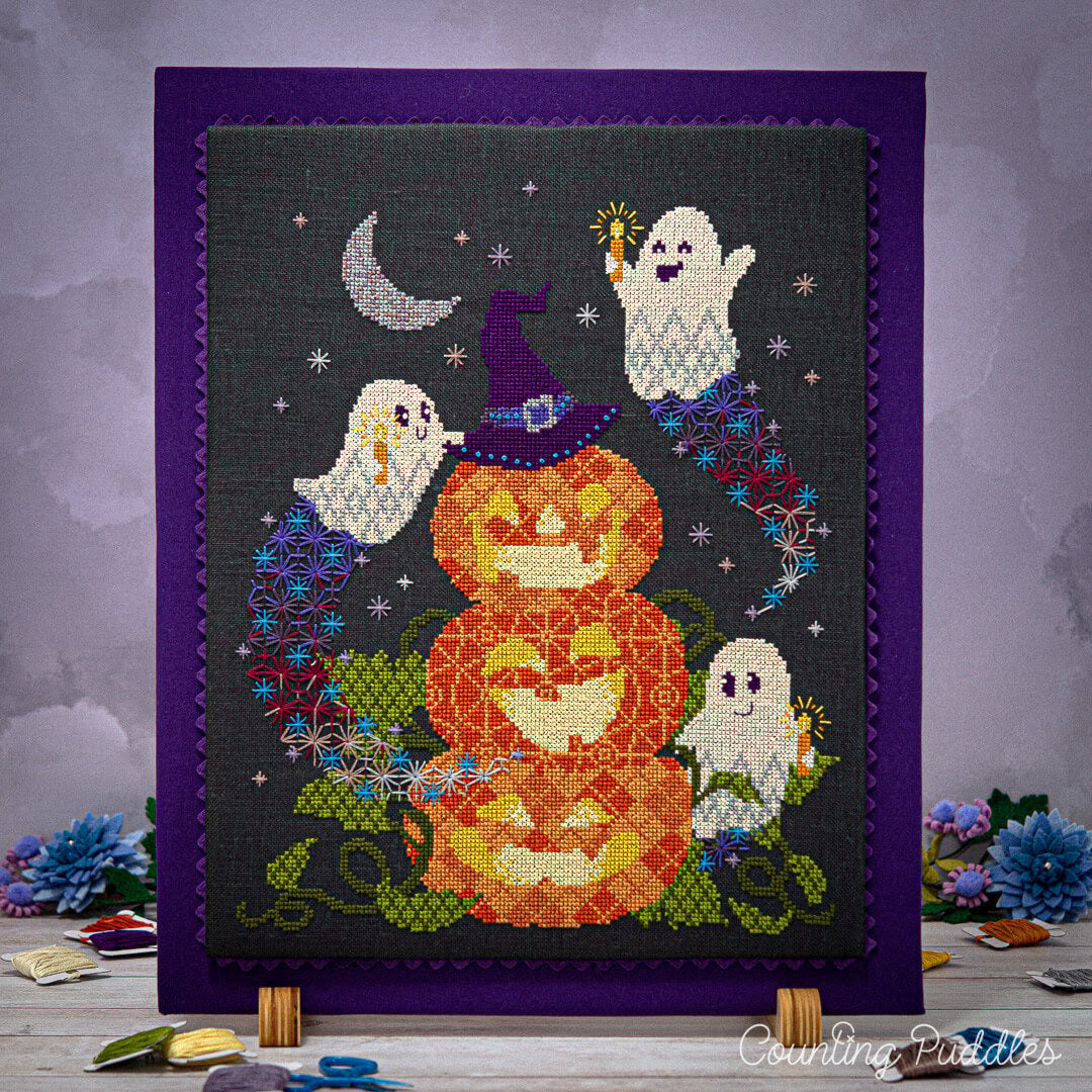 Cross-stitched Halloween design with pumpkins and ghosts on a dark background