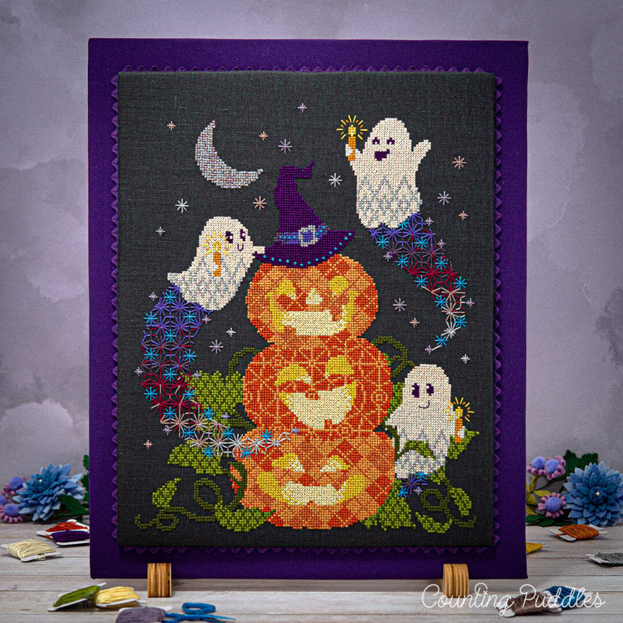Cross-stitched Halloween design with pumpkins and ghosts on a dark background