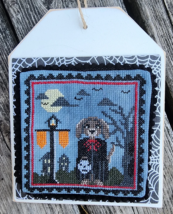 Decorative cross-stitched piece with a ghost and moon design on a wooden surface