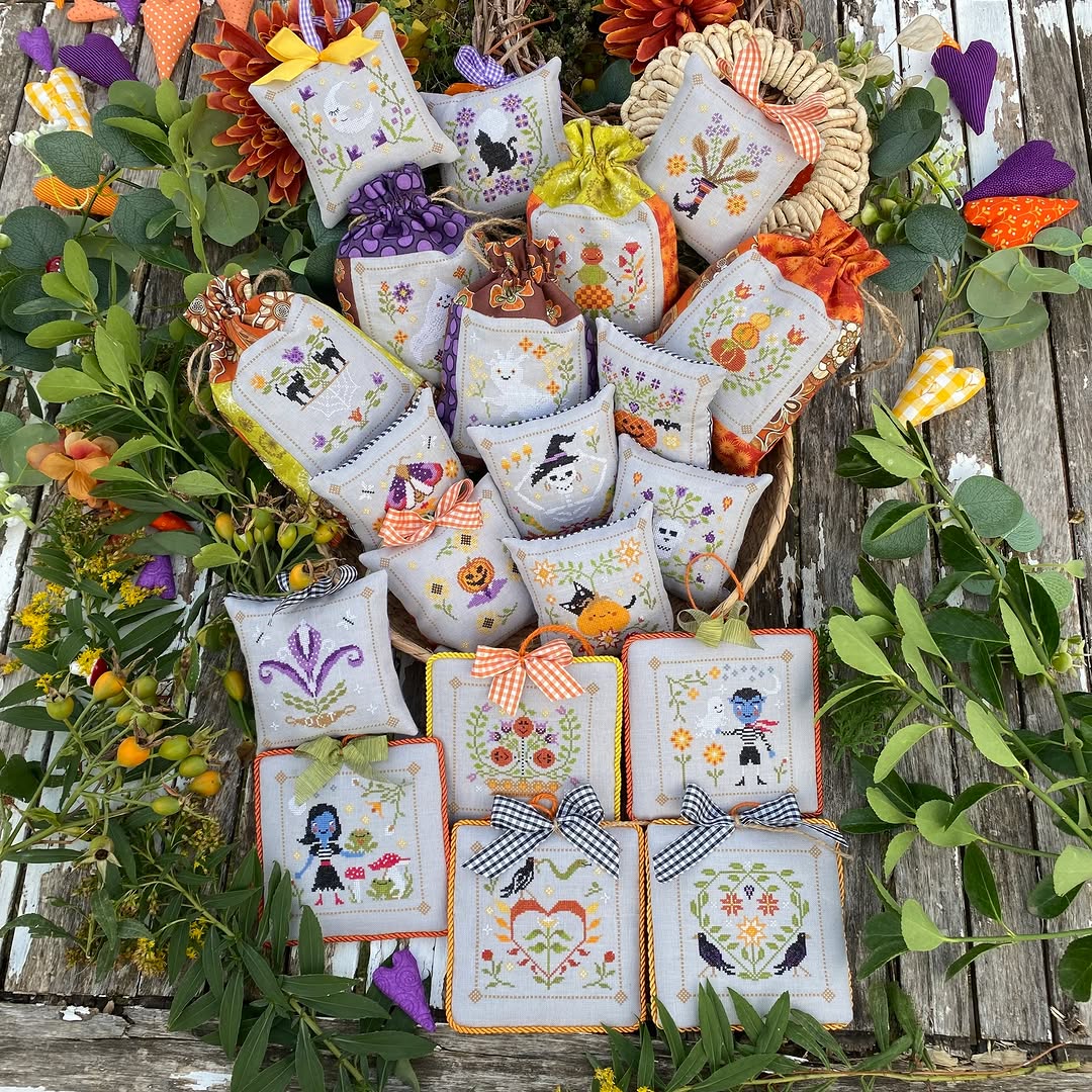 Collection of cross-stitched pillows with various designs on a wooden surface with greenery.