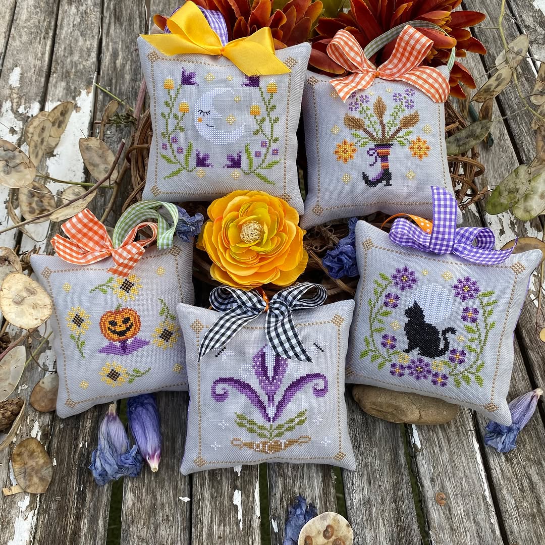 Decorative pillows with cross-stitch designs and colorful bows on a wooden surface.