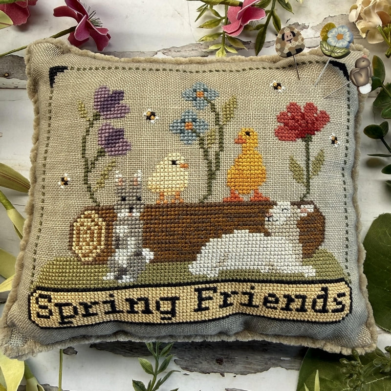 Decorative pillow with cross-stitched design of a dog, cat, and birds with flowers, labeled 'Spring Friends'.