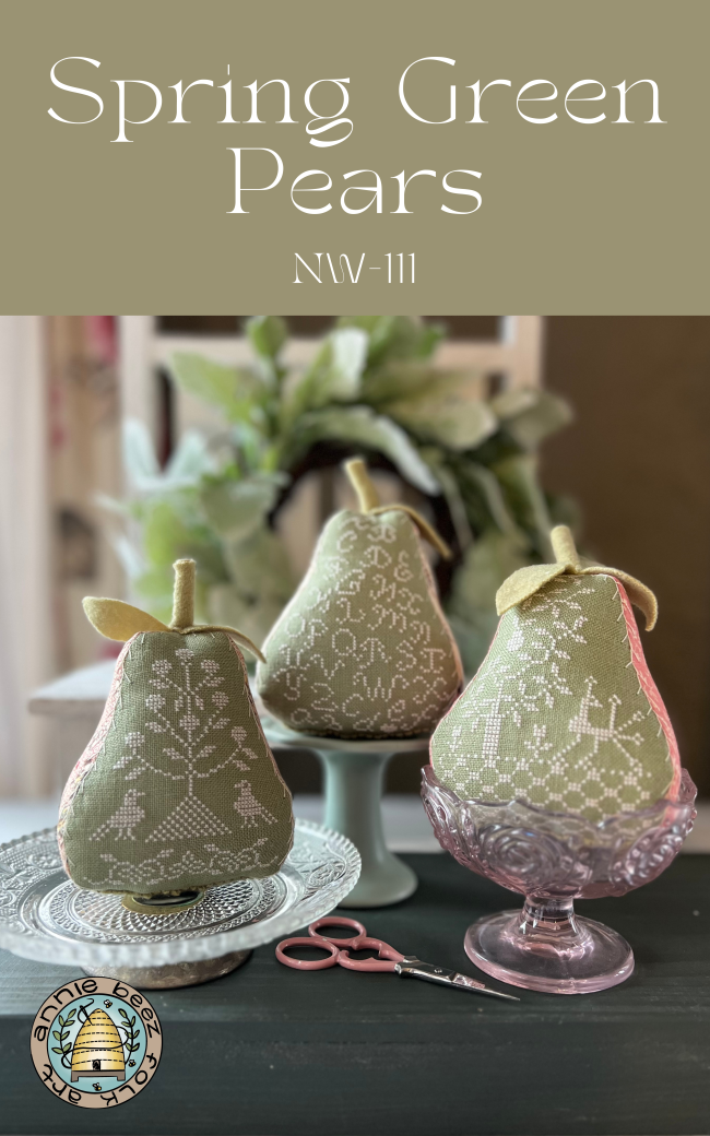 Three needlecraft kits depicting green pears with a floral pattern, displayed on a table with scissors and a needle and thread.