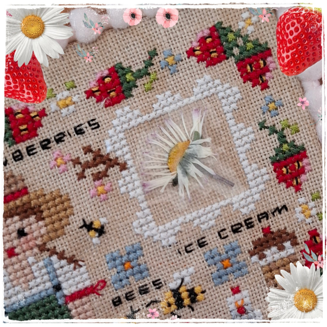 A square cross-stitch sampler featuring whimsical designs including a girl, strawberries, bees, daisies, and text reading 'BERRIES' and 'ICE CREAM' on a beige linen background.