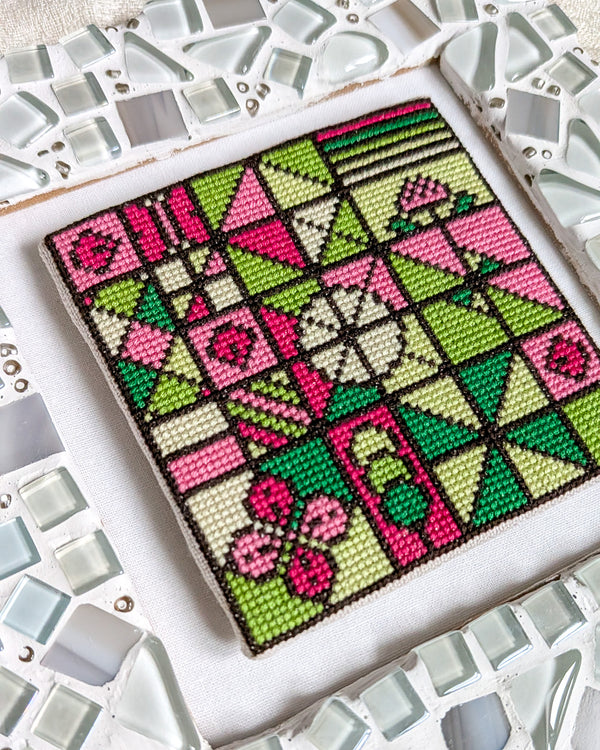 Cross-stitched pattern with pink and green geometric design on a white background