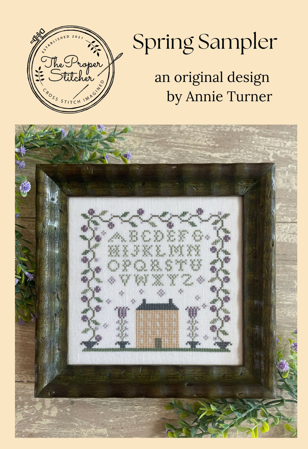 Spring Sampler cross-stitch design by Annie Turner with a wooden frame on a beige background.