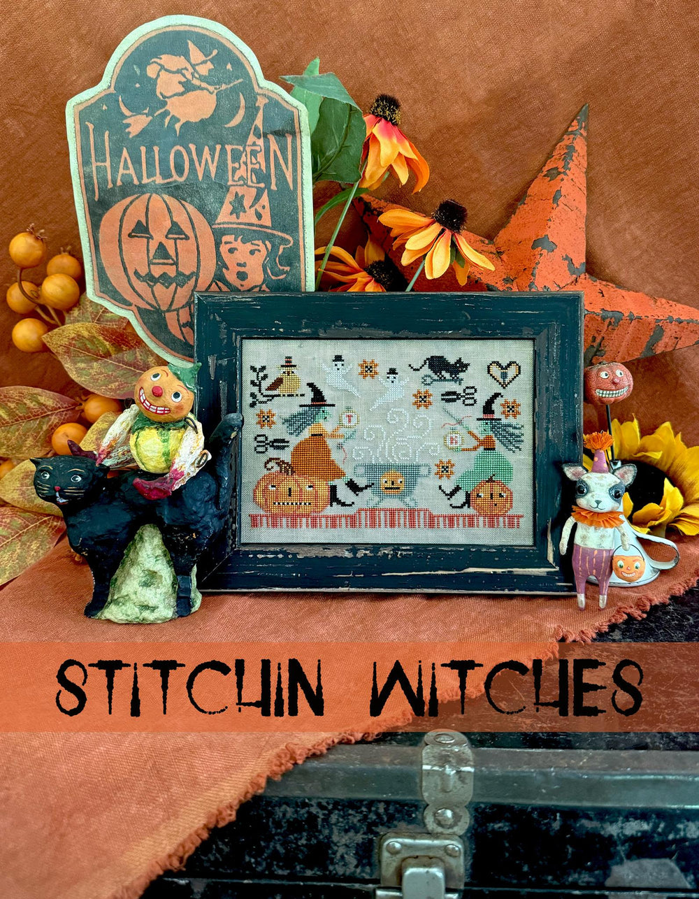 Halloween-themed decor with a cross-stitch pattern, pumpkins, and decorative items on a brown background.