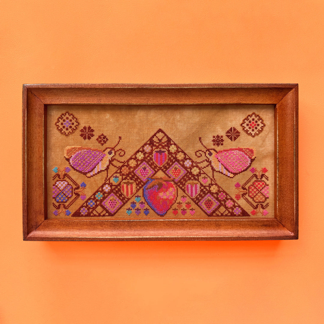 Framed cross-stitched artwork with geometric patterns and hearts on an orange background