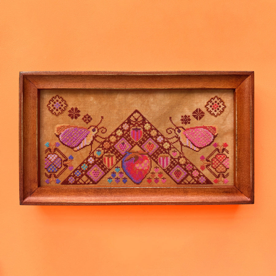 Framed cross-stitched artwork with geometric patterns and hearts on an orange background