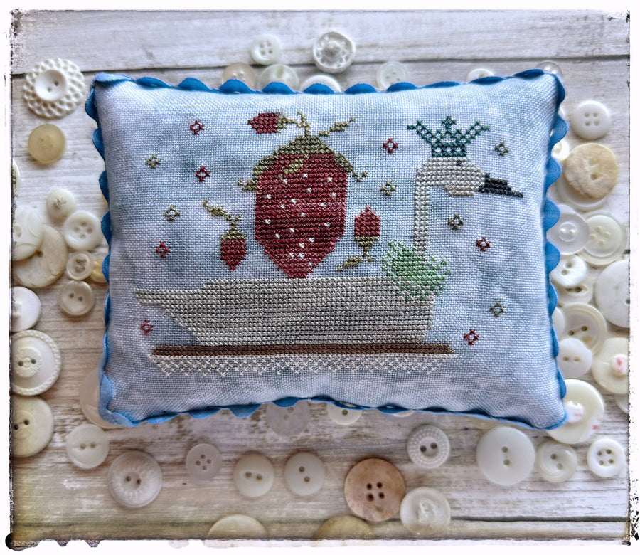 Cross-stitched pillow with strawberry design on a wooden surface with buttons