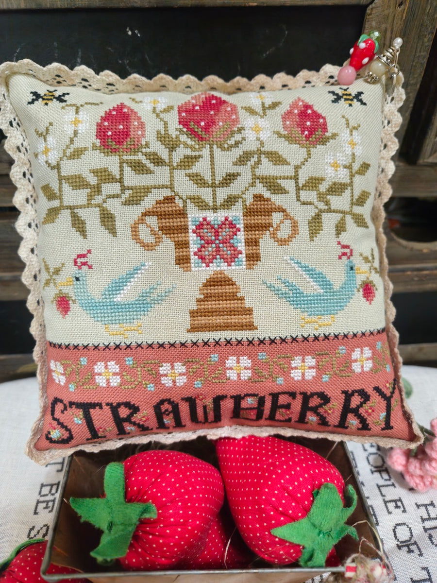 Decorative pillow with cross-stitched design and strawberries on a wooden surface