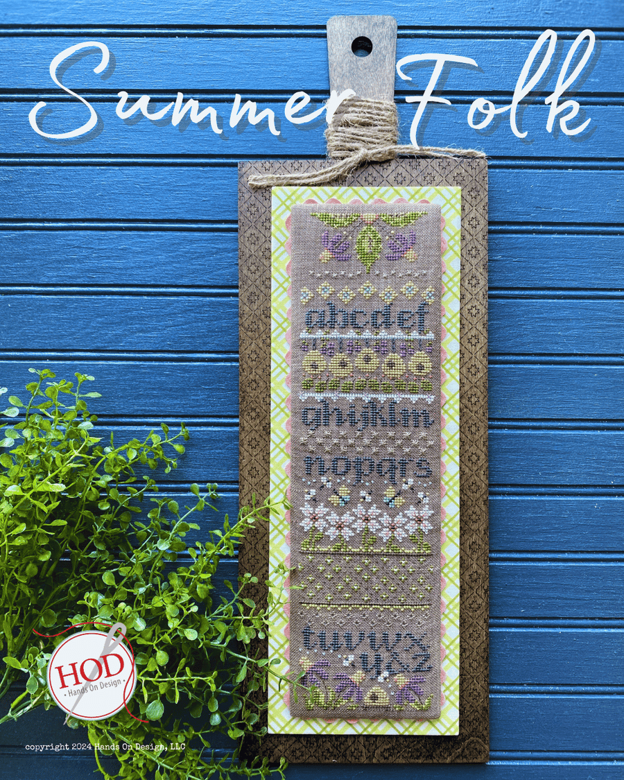 Cross-stitched bookmark with decorative text and patterns on a blue background, featuring the brand 'HOD'.