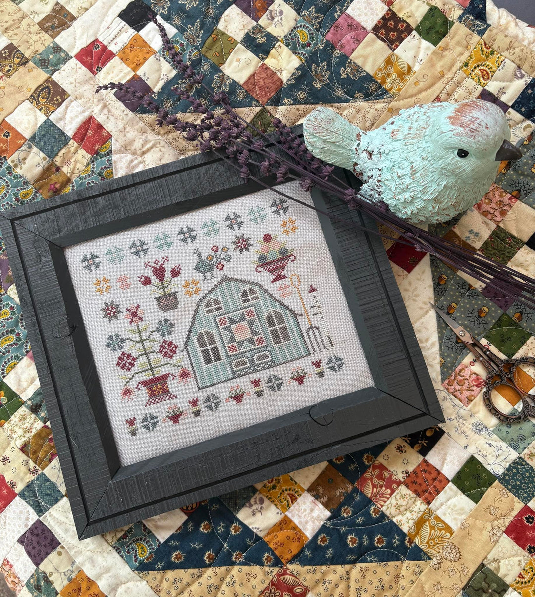 Framed cross-stitched design of a house on a quilted fabric background