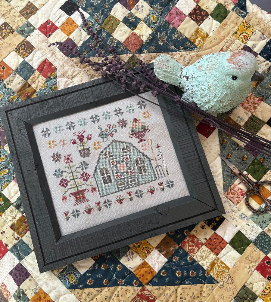 Framed cross-stitched design of a house on a quilted fabric background