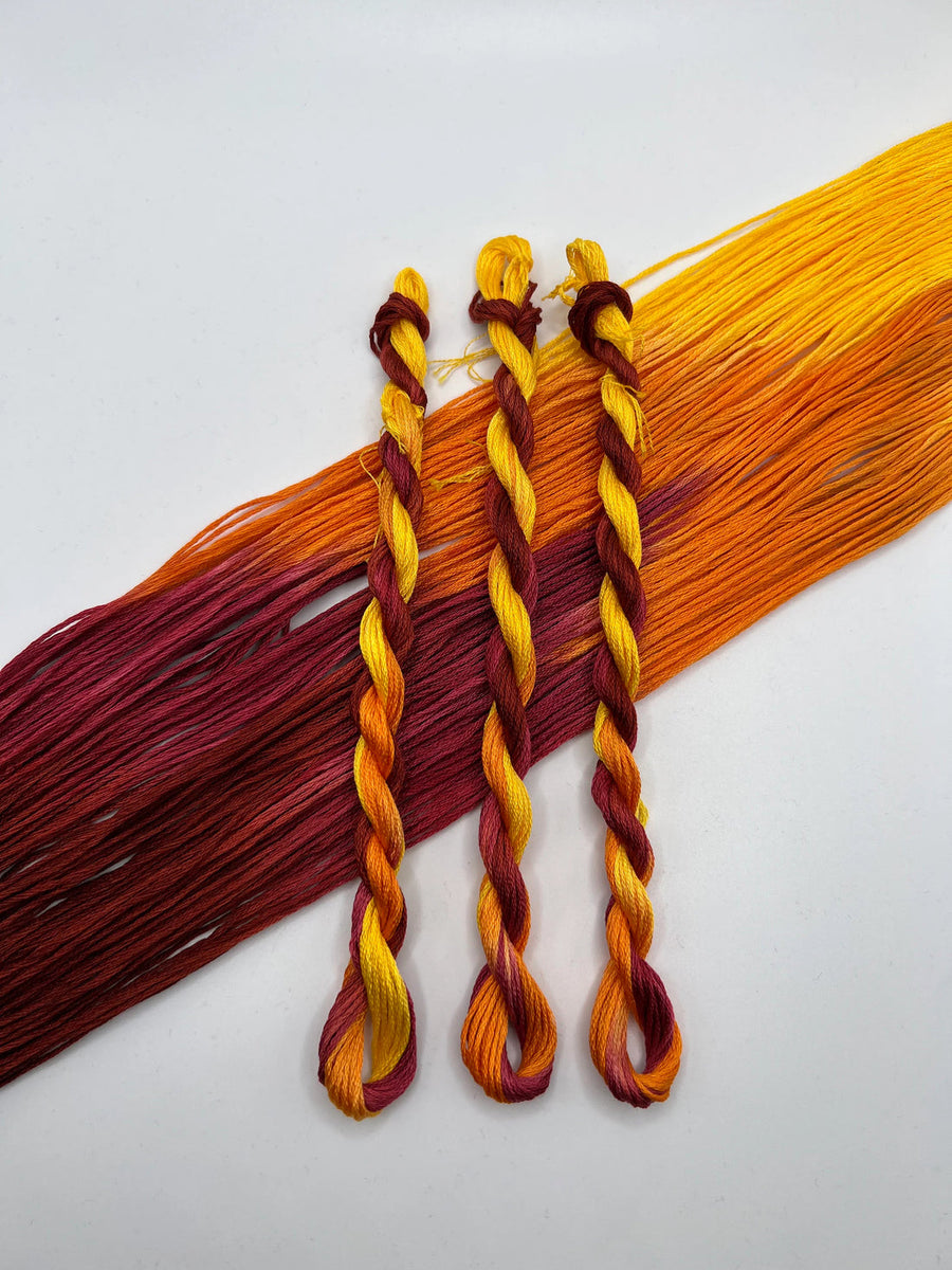 Three braided strands of red, yellow, and orange yarn on a white background