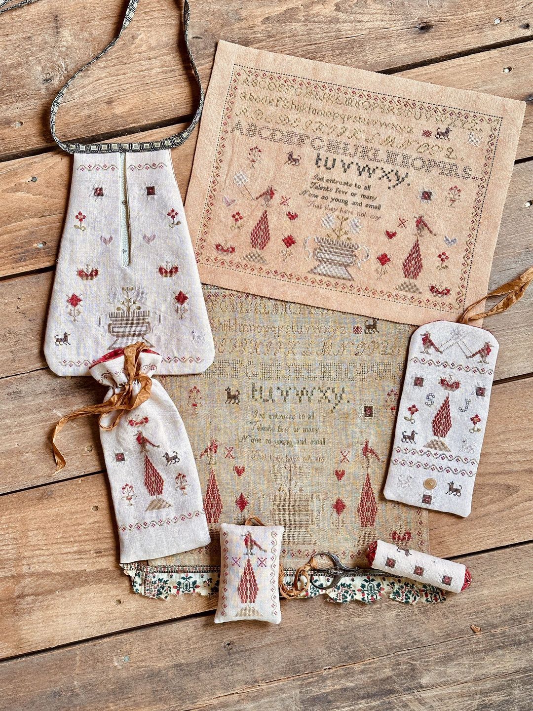 Cross-stitched fabric pieces and a sampler on a wooden surface