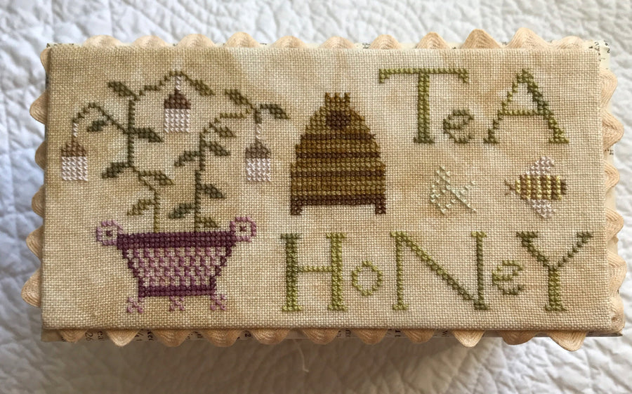 Cross-stitched panel with bee, honeycomb, and text on a textured fabric background