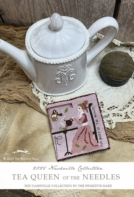 White teapot with a cross-stitched needlebook featuring 'Tea Queen of the Needles' design on a textured surface.