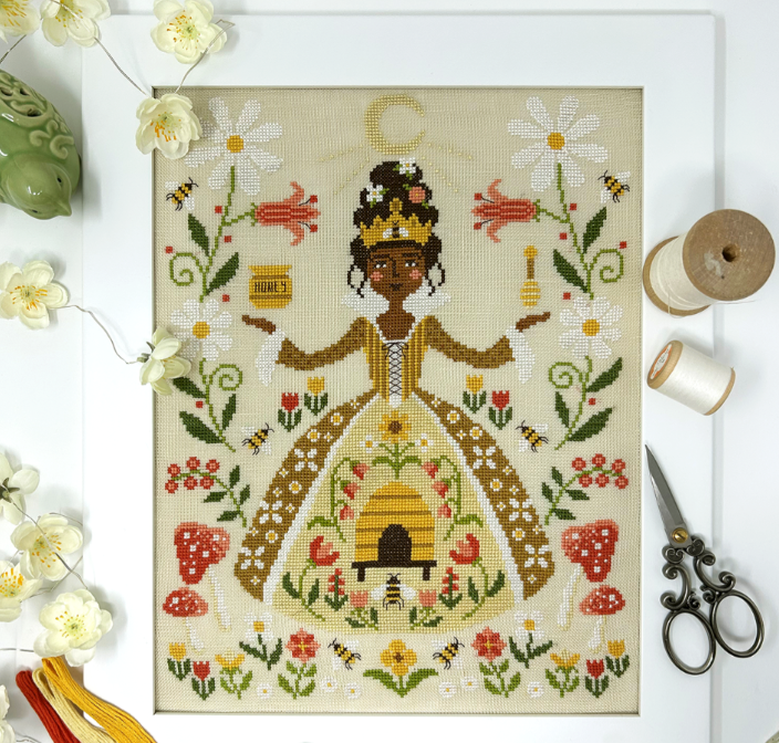 Cross-stitched picture of a woman in a floral dress with bees and flowers on a white background.