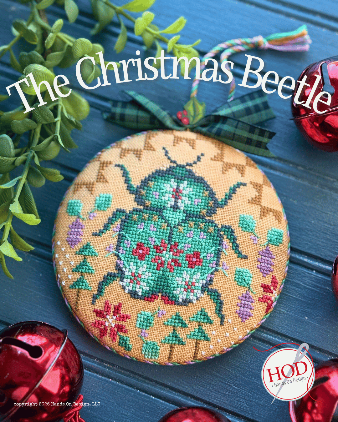 A round embroidered Christmas ornament featuring a green beetle with red and white floral details on a tan background, decorated with a dark green plaid ribbon. The ornament is displayed on a dark blue wooden surface with red holiday ornaments and green foliage around it.