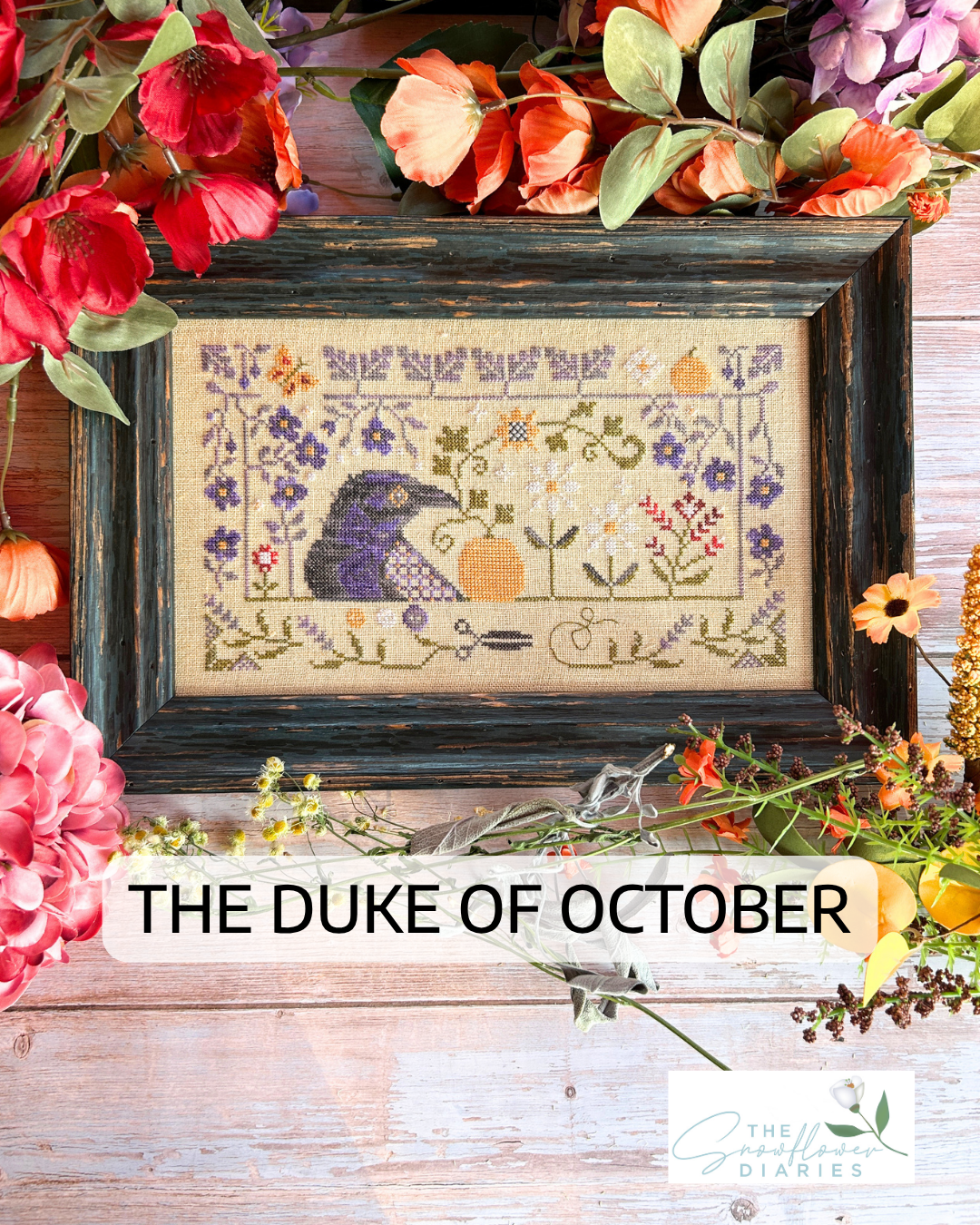 A framed cross-stitch artwork featuring a purple duck and autumn floral motifs on a beige fabric background, styled with colorful flowers around it on a rustic wood surface. Text overlay reads 'THE DUKE OF OCTOBER' and the brand 'The Smallest Diaries' appears at the bottom right.