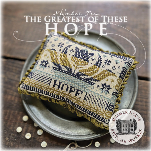 Decorative pillow with cross-stitch design and 'HOPE' text on a wooden surface, featuring Summer House Stitche Works logo.